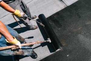 A homeowner compares a new asphalt shingle sample with weathered shingles on a sloped roof.