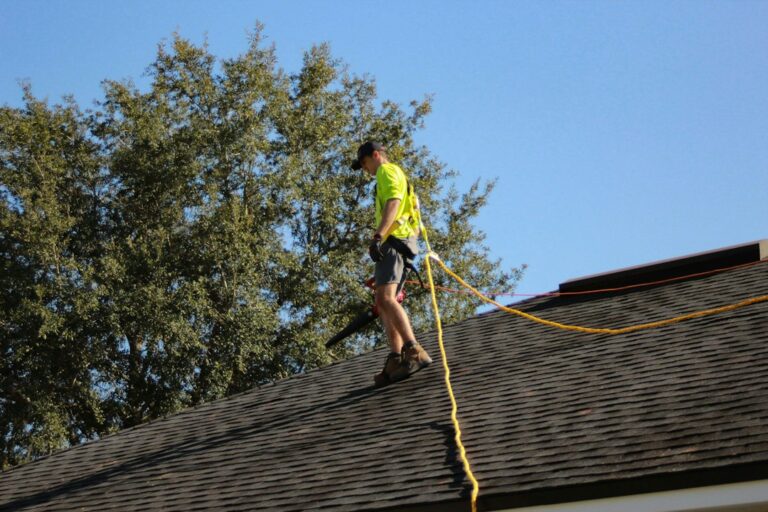 Homeowner inspecting roof edges with binoculars while a ladder, gloves, tools, and gutter scoop rest nearby.